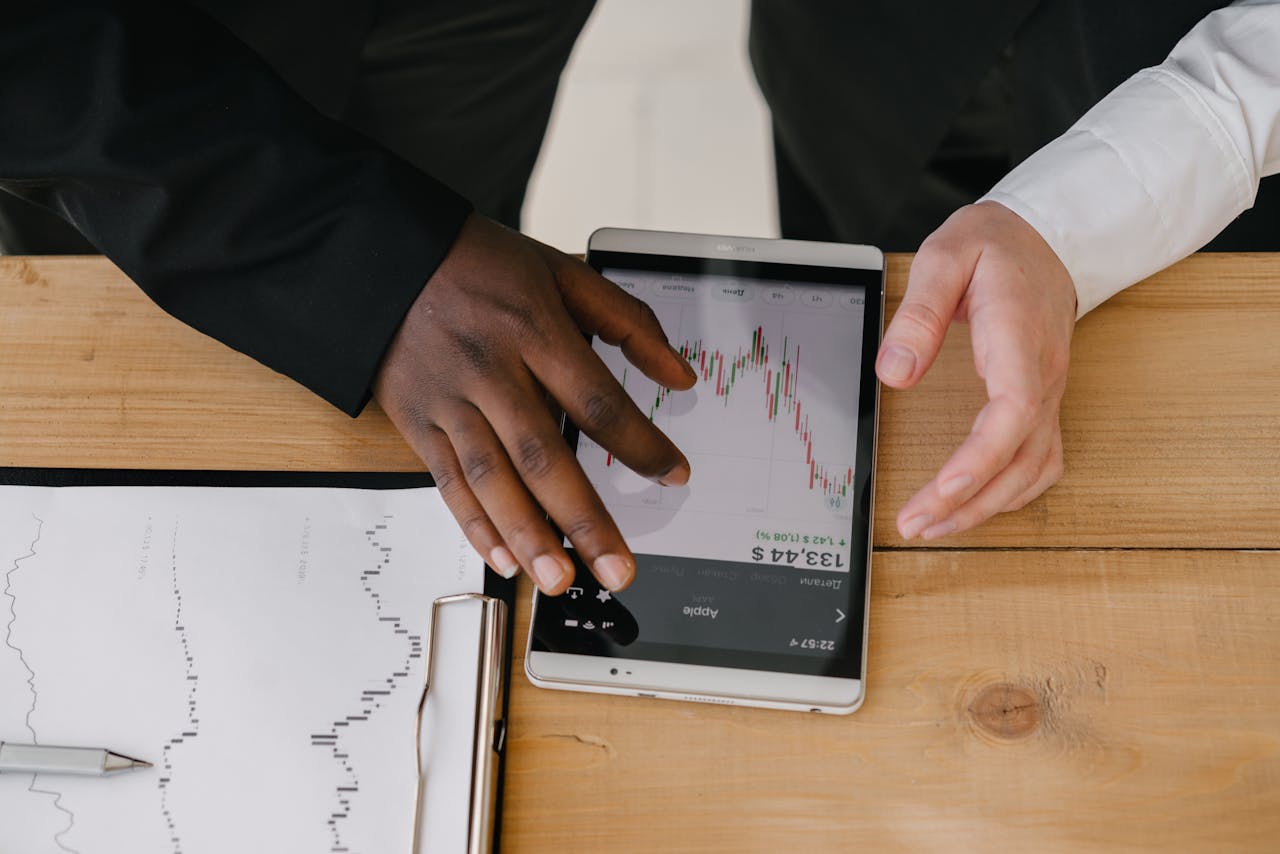 Two professionals analyzing stock market trends on a tablet in an office setting.