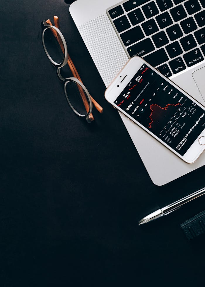 Close-up of a smartphone displaying stock market data next to a laptop and eyeglasses.